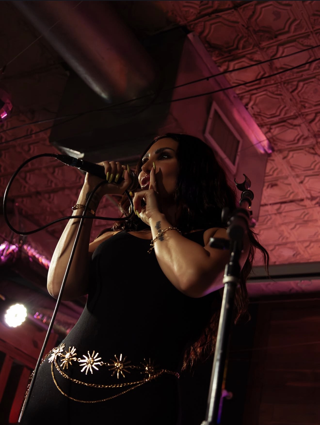 Jada Davino performing beneath a pink-lit pressed tin ceiling