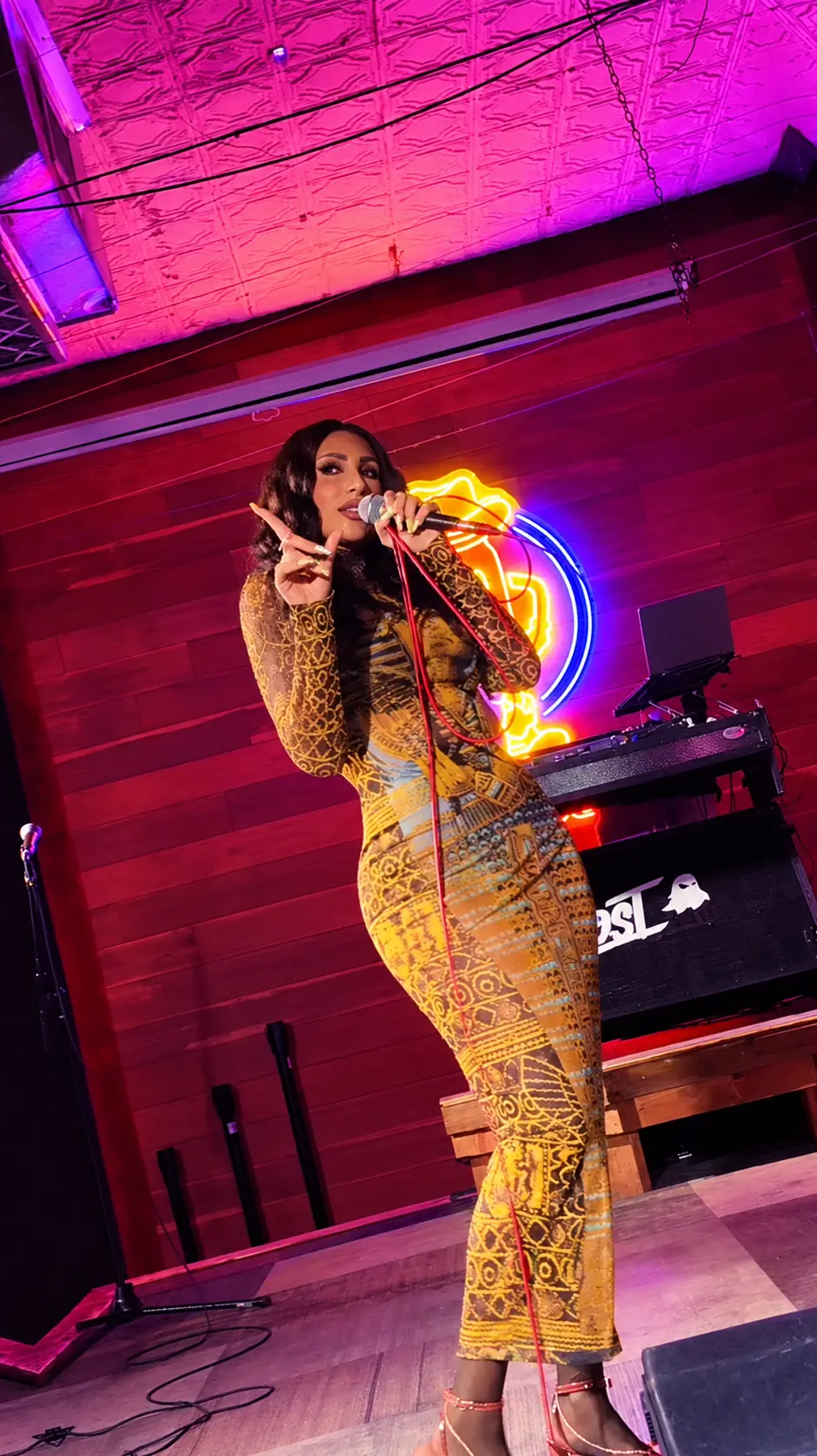 Jada Davino performing in a gold print dress beside a neon sign